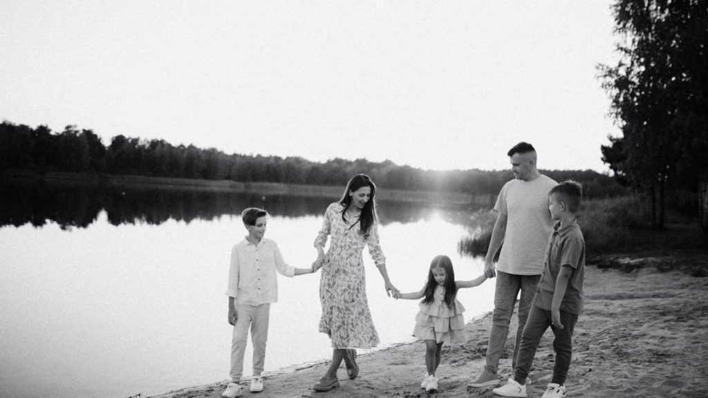 Monochrome photo of a family walking hand in hand along a serene lakeshore.