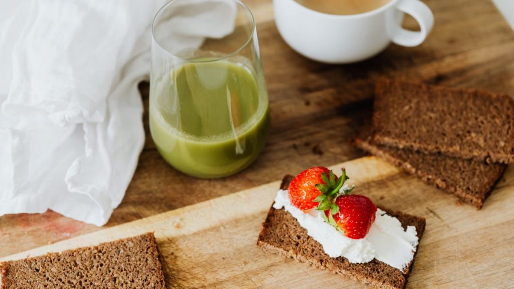 Start your day with a nutritious breakfast featuring rye toast with cream cheese and strawberries, paired with green juice and coffee.